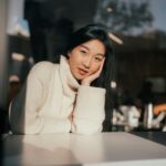 Home A woman in a cozy sweater enjoying sunlight at a café table in San Francisco.